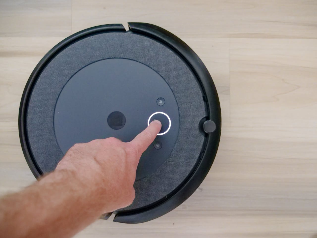 hero-img-01 Close-up of a finger pressing a start button on a robotic vacuum cleaner at home.